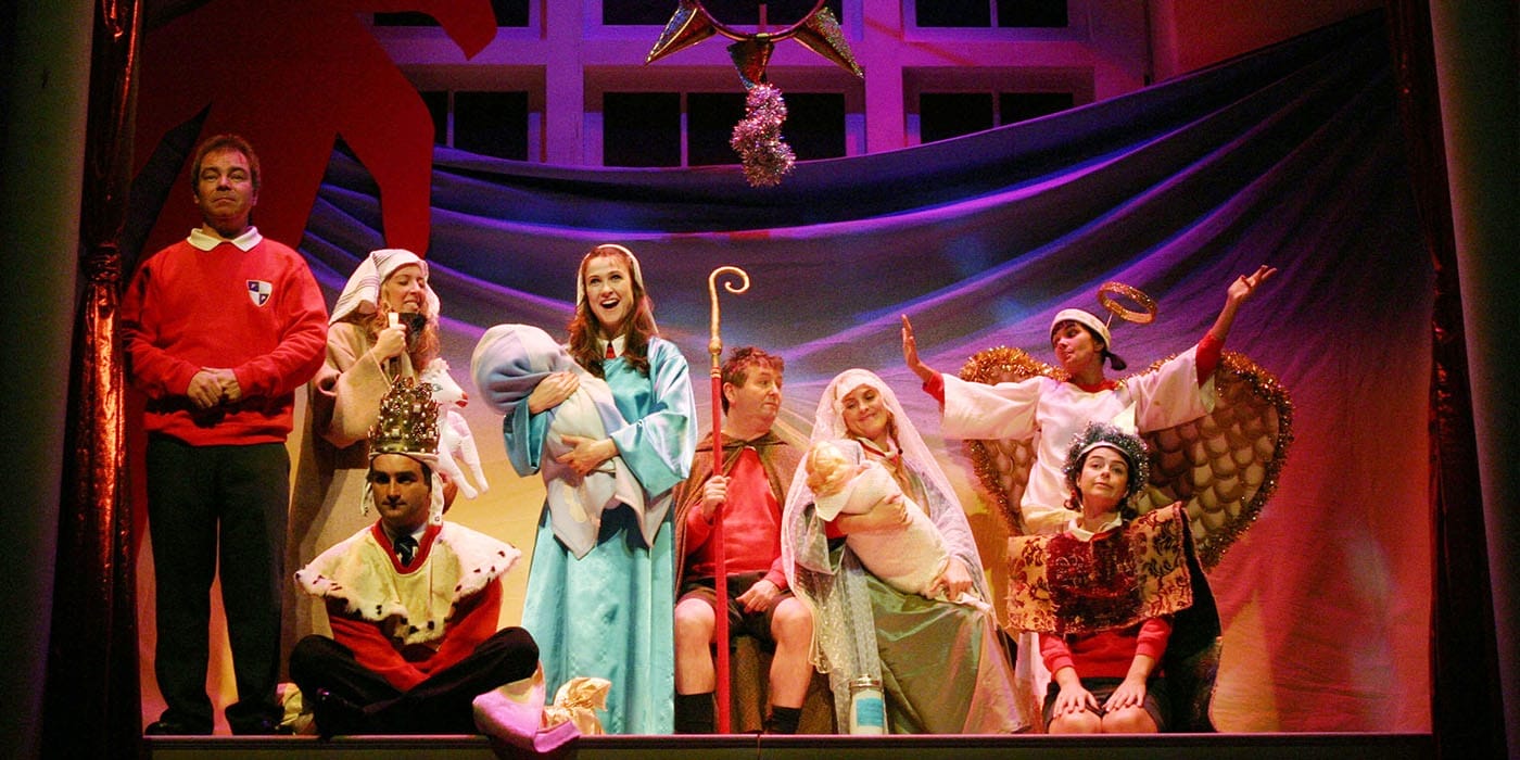 The cast dressed as the nativity characters with red primary school uniforms underneath peering out.