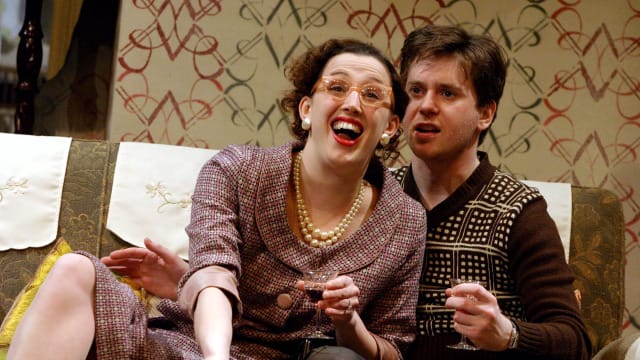 A man sat on a sofa and a woman sat infront of him looking joyous