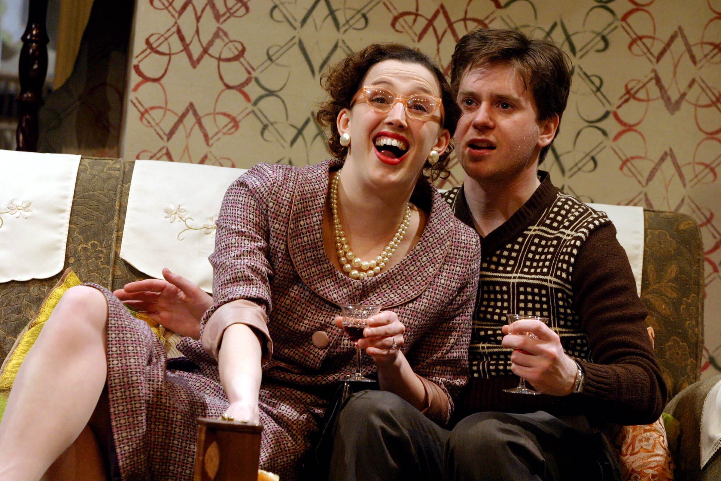 A man sat on a sofa and a woman sat infront of him looking joyous