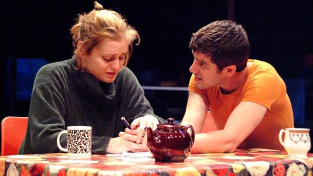 A man and woman sat at the table talking. The woman is crying.