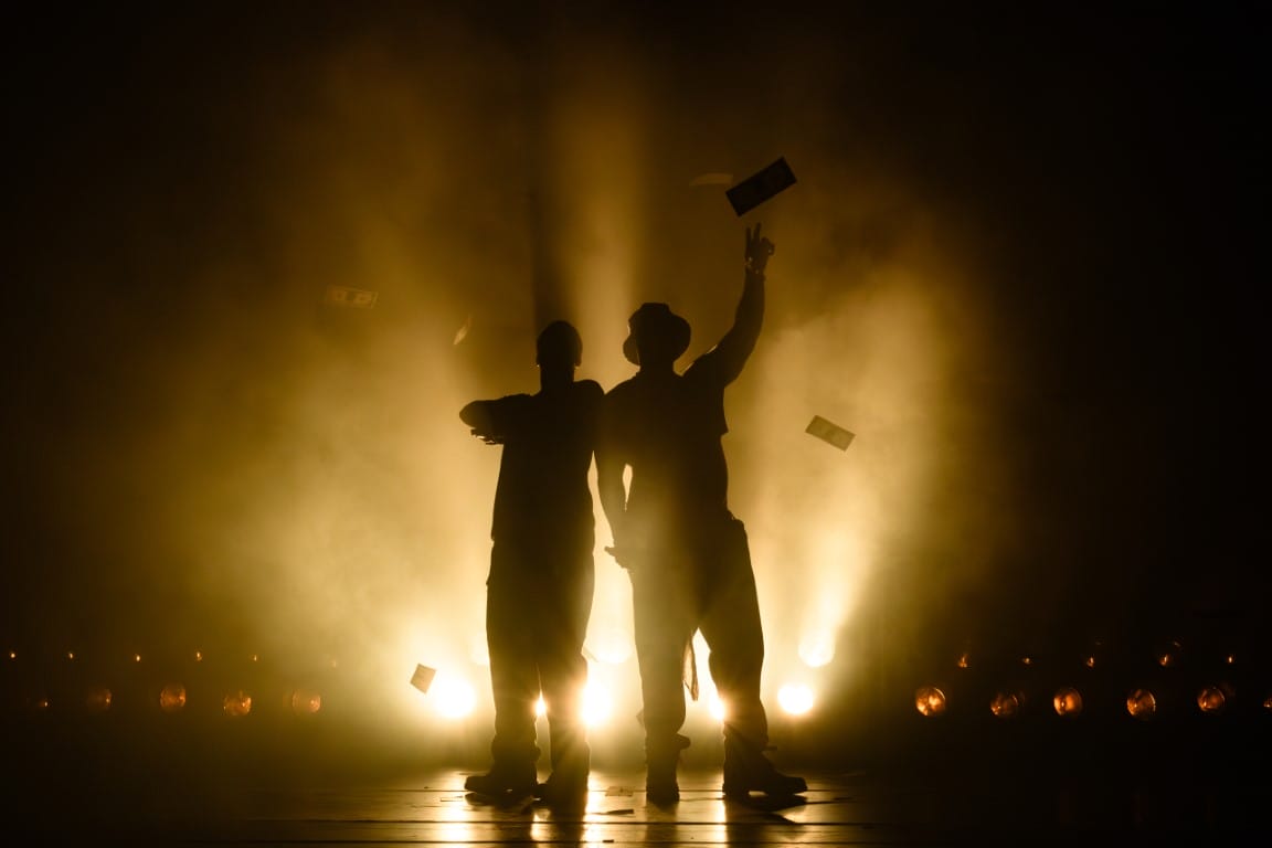 A silhouette of two men with money dropping behind