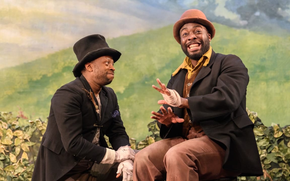 Two men sat in a field with formal dress and top hats on.